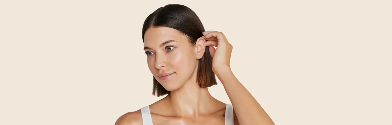 Porträt einer Patientin, die sich die Haare hinter das am Kopf anliegende Ohr streicht.